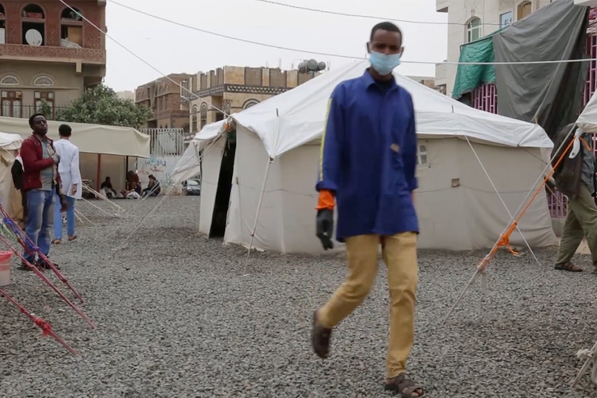 A man wearing a surgical mask walks through a car park in Yemen where people are being treated for cholera.