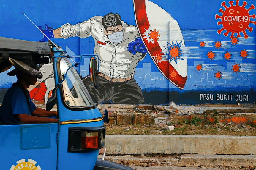 A rickshaw taxi passes a mural promoting awareness of the coronavirus disease in Jakarta.