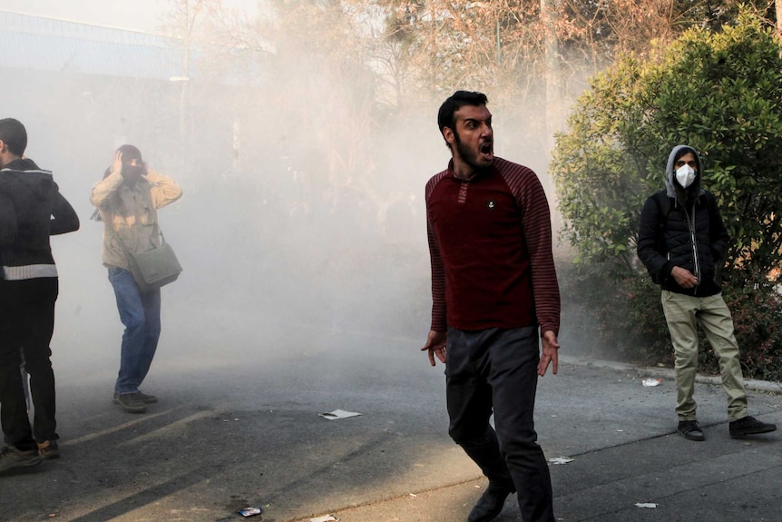 A man, standing in a cloud of smoke in the street, yells.