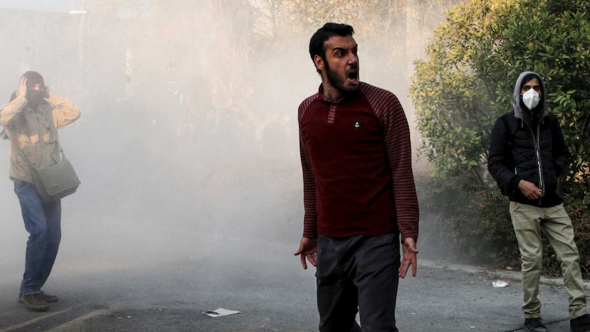 A man, standing in a cloud of smoke in the street, yells.