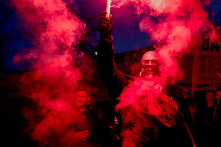 People burn red bengalos as they take part in a demonstration.