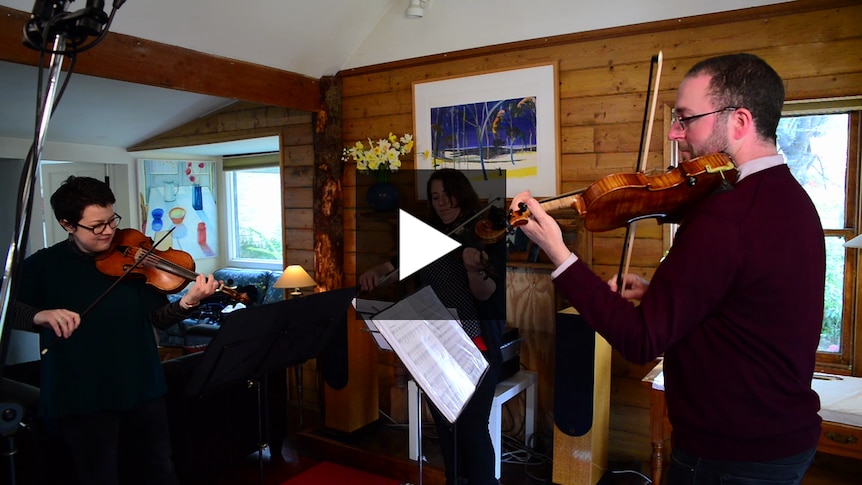 Three fiddlers perform violin in a living room.