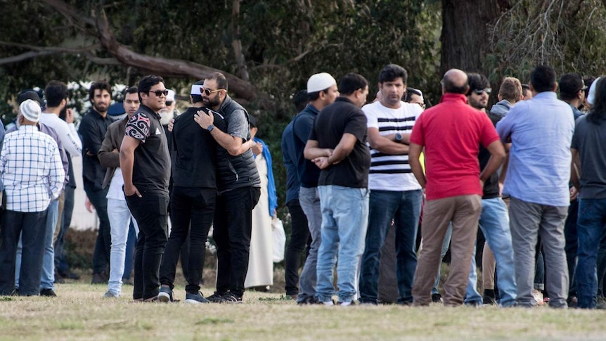 Mourners at a cemetery hug and speak to each other.