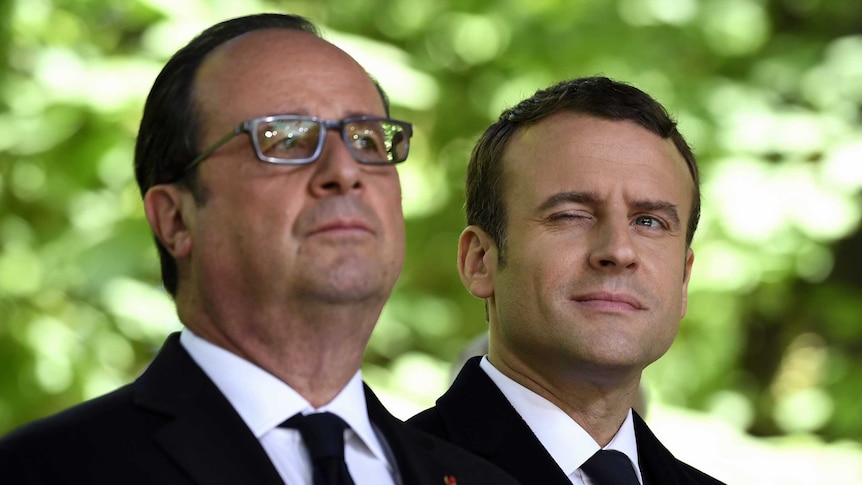 Emmanuel Macron winks as he stands beside outgoing French President Francois Hollande.