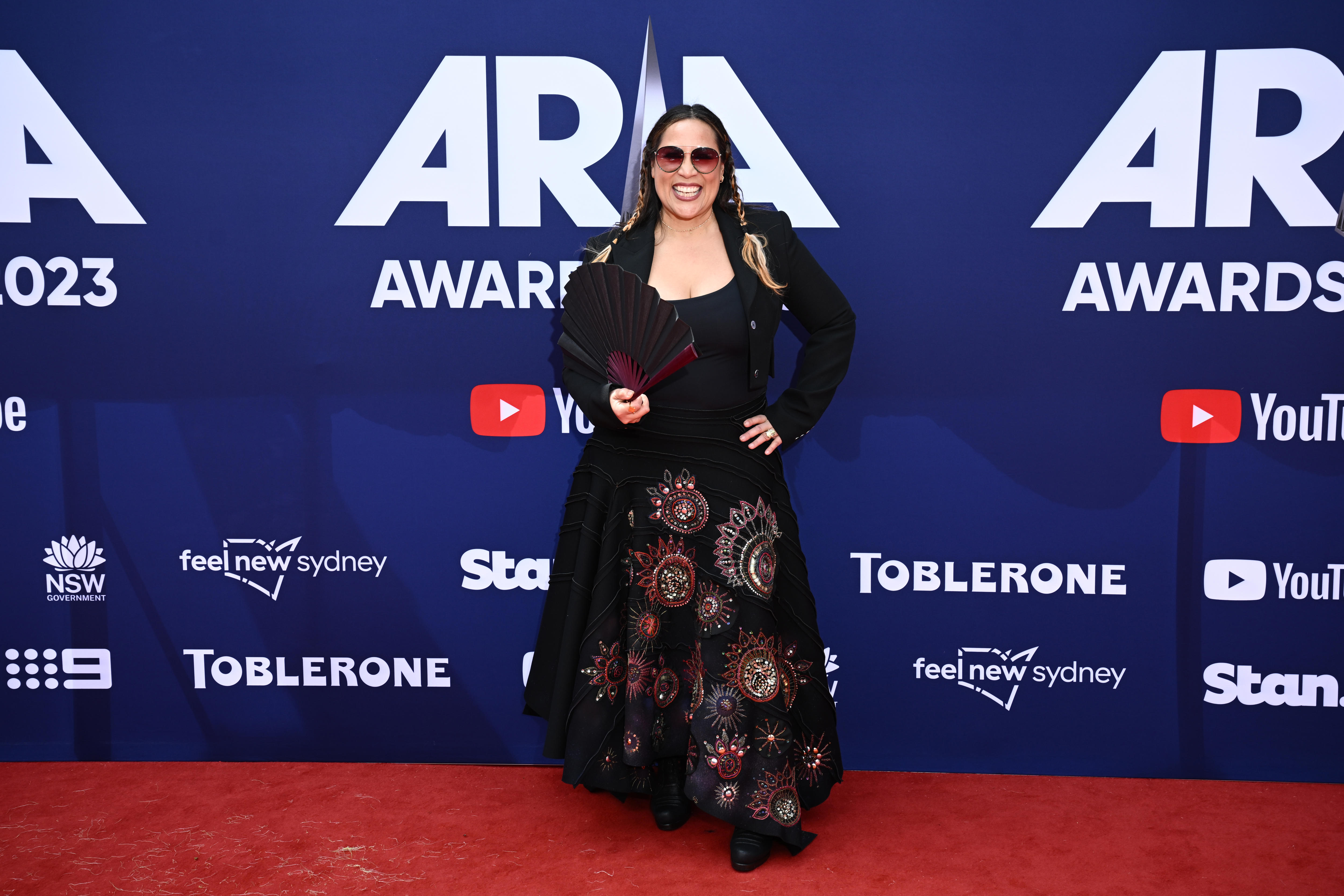 A lady wearing a black dress with patterns and is holding a fan