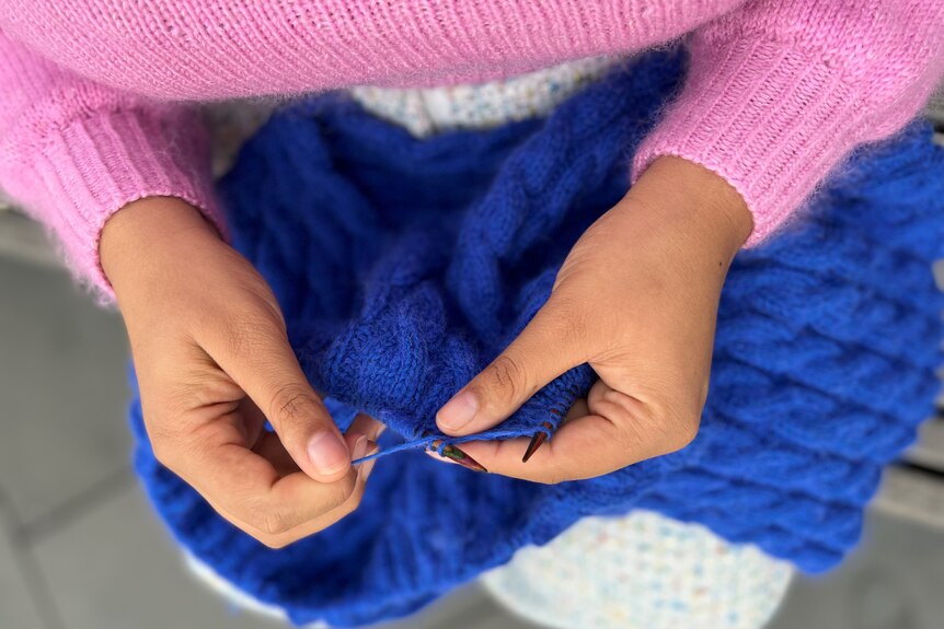 Yasmin is seen knitting in an image shot from above. She wears a pink jumper she made.