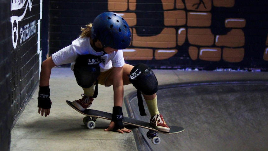 A young girl balances on her skateboard, readying herself to head back into the bowl.