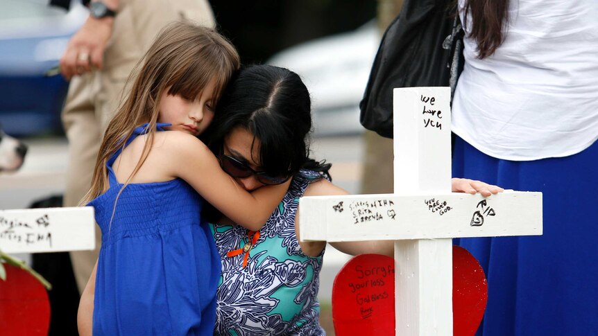 A woman holds her daughter in front of the row of crosses at a memorial in Virginia Beach.