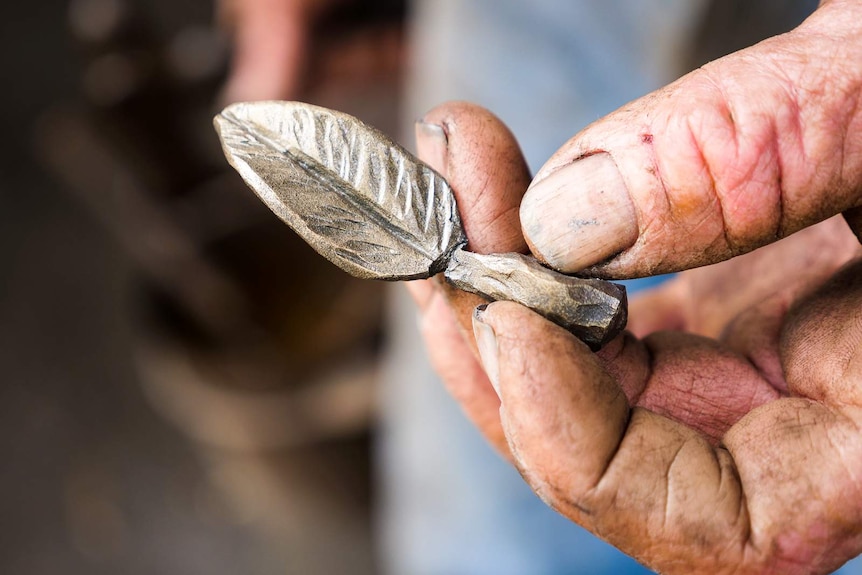 a man's hand is holding a piece of metal shaped into a feather ornament