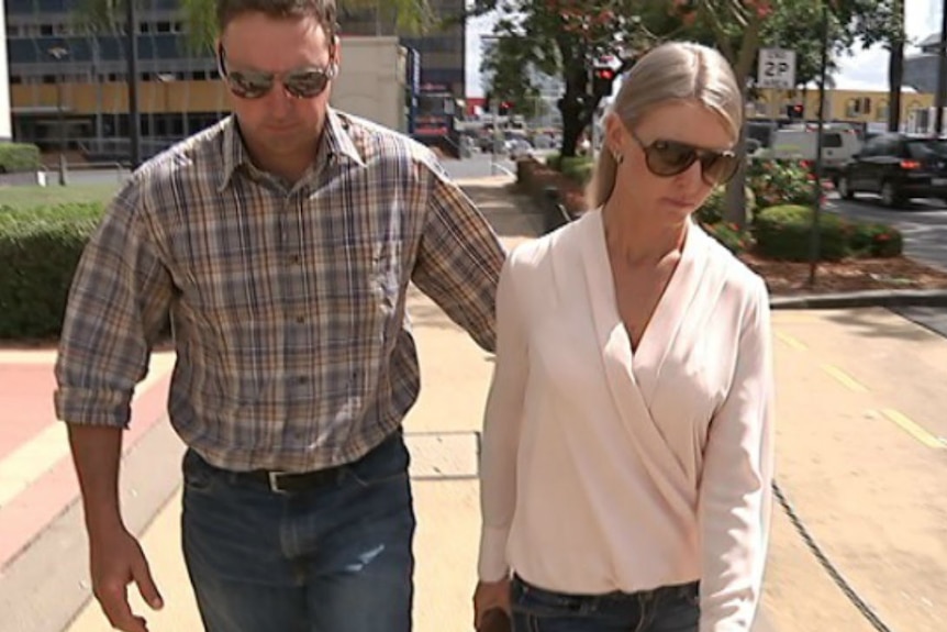 man and woman wearing sunglasses and looking down walking along street