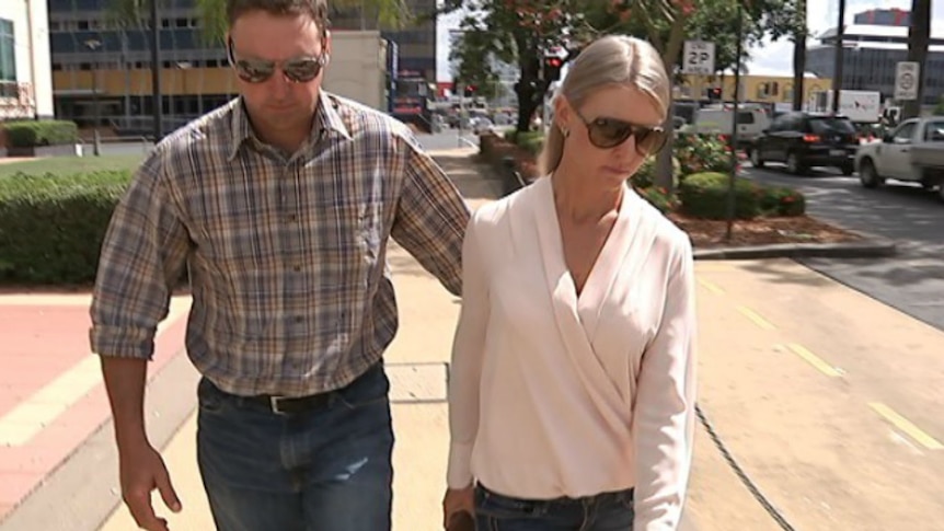 man and woman wearing sunglasses and looking down walking along street