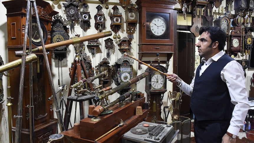 Man stands in a room with hundreds of clocks.