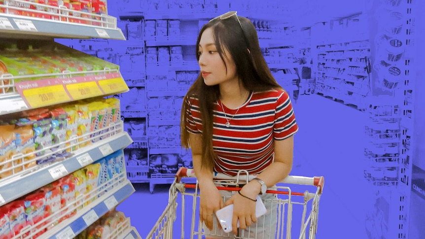 A woman pushes a trolley in a supermarket for a story about how to avoid buying unhealthy food when grocery shopping.