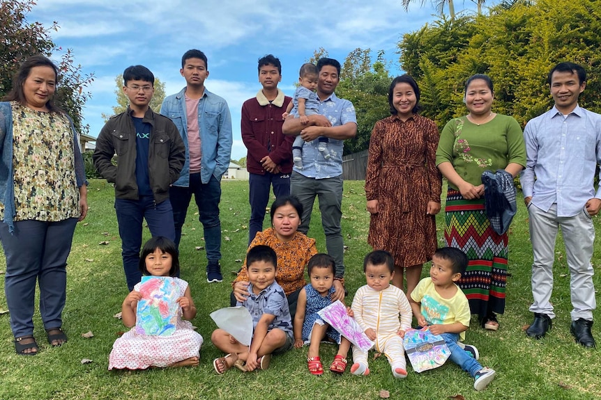 A group of men, women and children in a western and Myanmar clothes in a park.