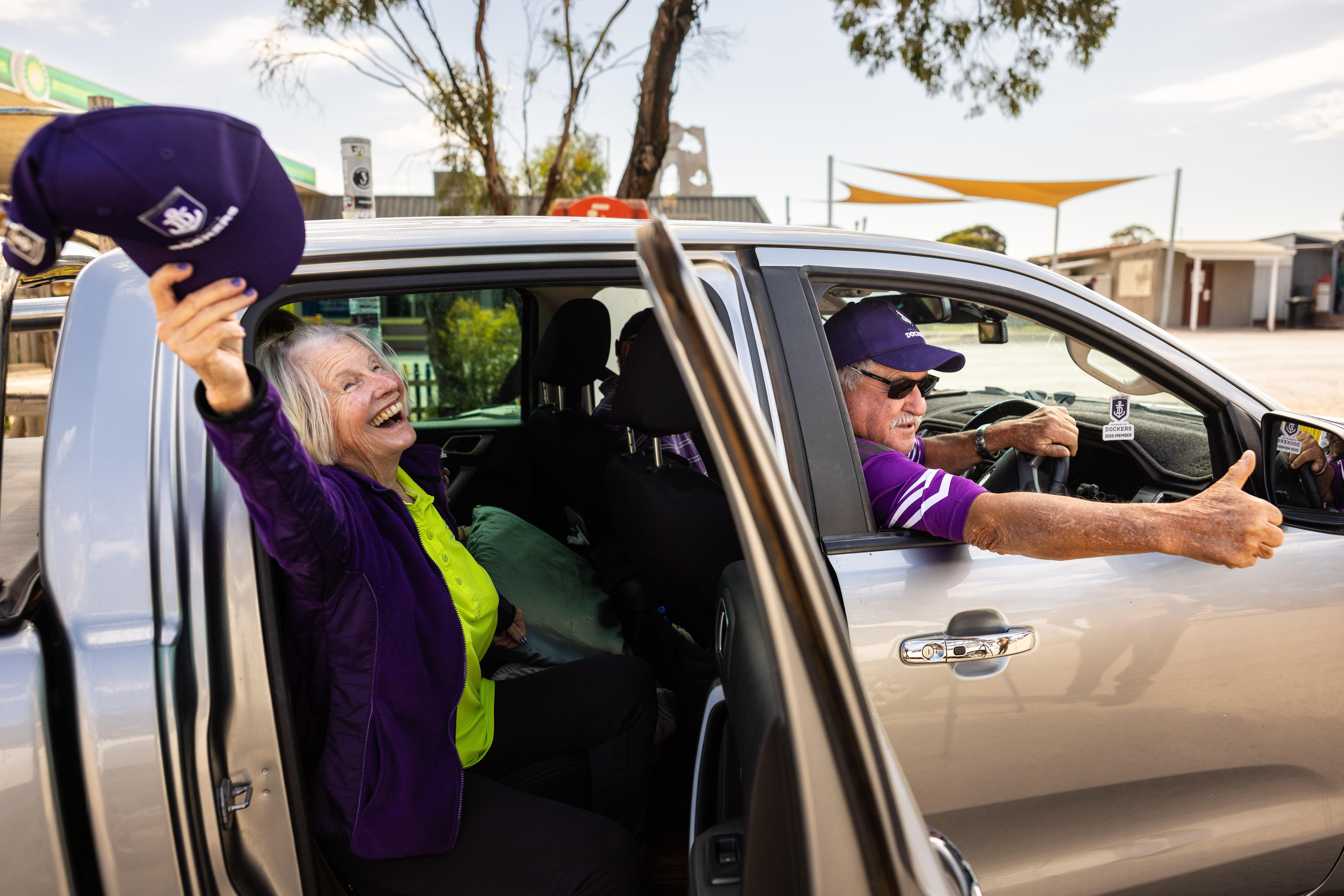 A woman waves goodbye with her Fremantle hat as a car prepares to drive off.