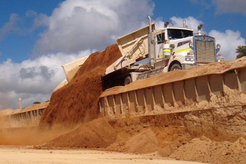 A truck dumps its load from the side of its tray on Christmas Island.