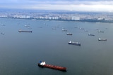 A sea with many cargo ships anchored in front of a city
