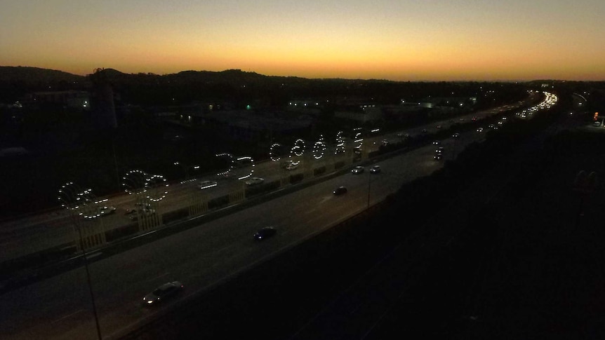 An aerial shot soon after sunset depicting a highway and a sign in lights that spells Gold Coast.