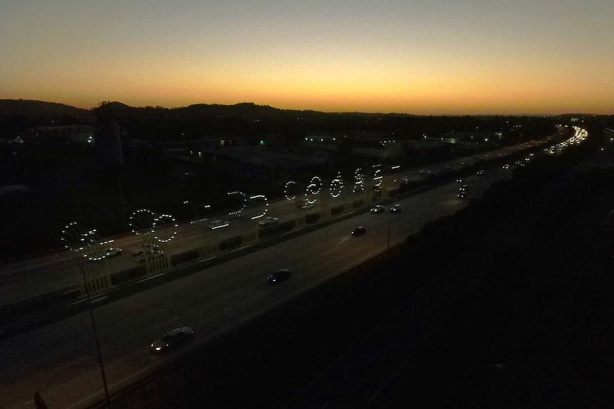 An aerial shot soon after sunset depicting a highway and a sign in lights that spells Gold Coast.