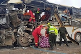 A bus that has been wrecked into twisted steel and torn apart, which is being searched by emergency workers