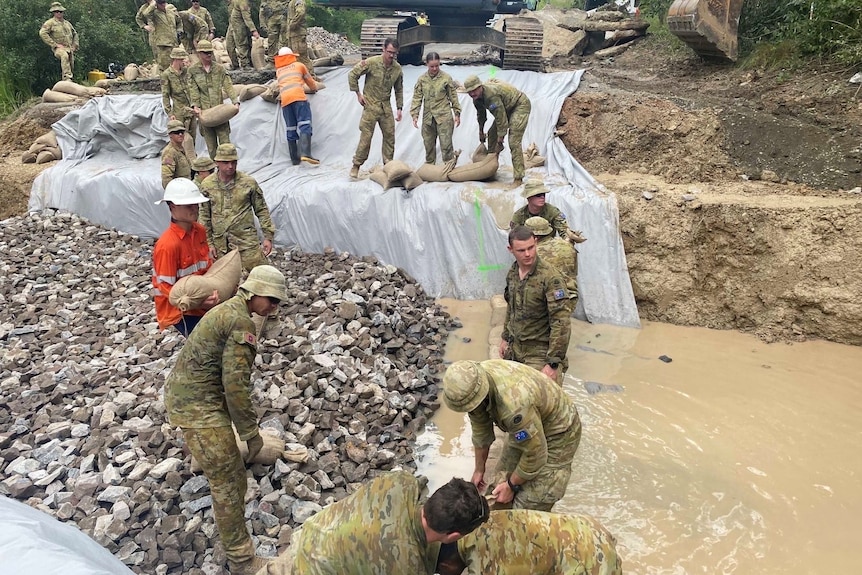 army personel carrying sand bangs to make an embankment agaisnt flood waters
