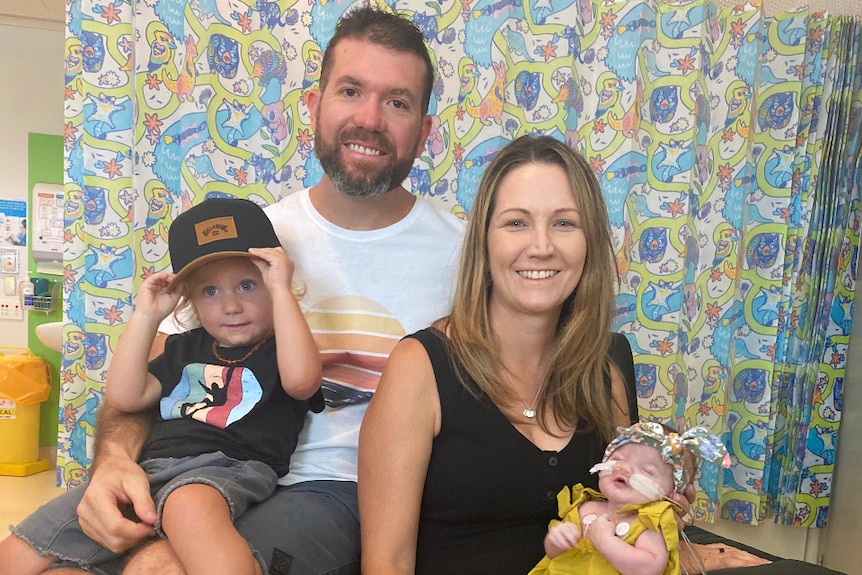 Parents with two young children smile while sitting on an armchair.