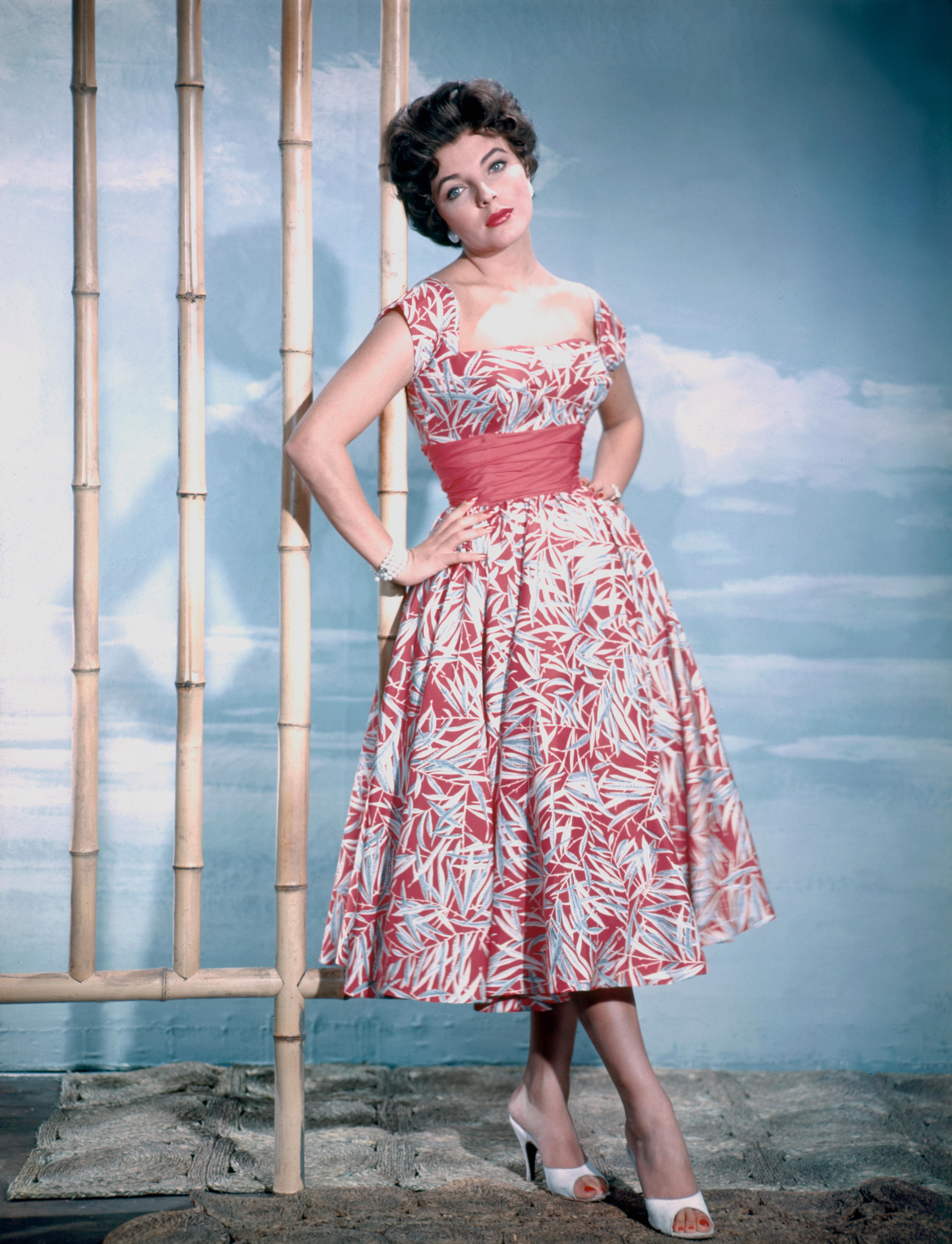 A beautiful white woman with short brown hair and blue eyes wears a classic 50s dress in red and blue.