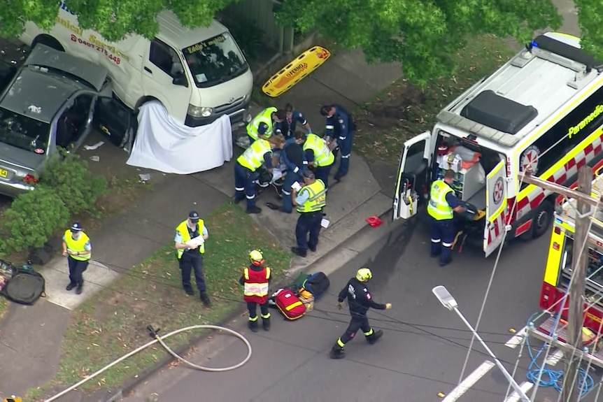 An aerial view of two cars which have collided with paramedics huddled around a stretcher 