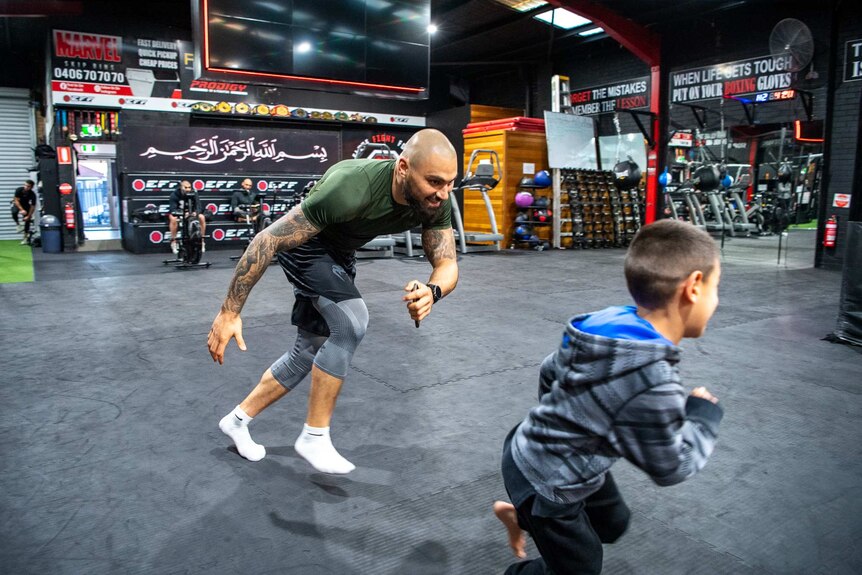 A man and child run on a mat at a gym.