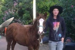 A young woman stands next to a horse.