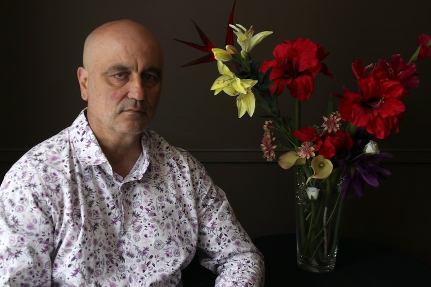 Gerry sits at a table next to a vase of flowers.