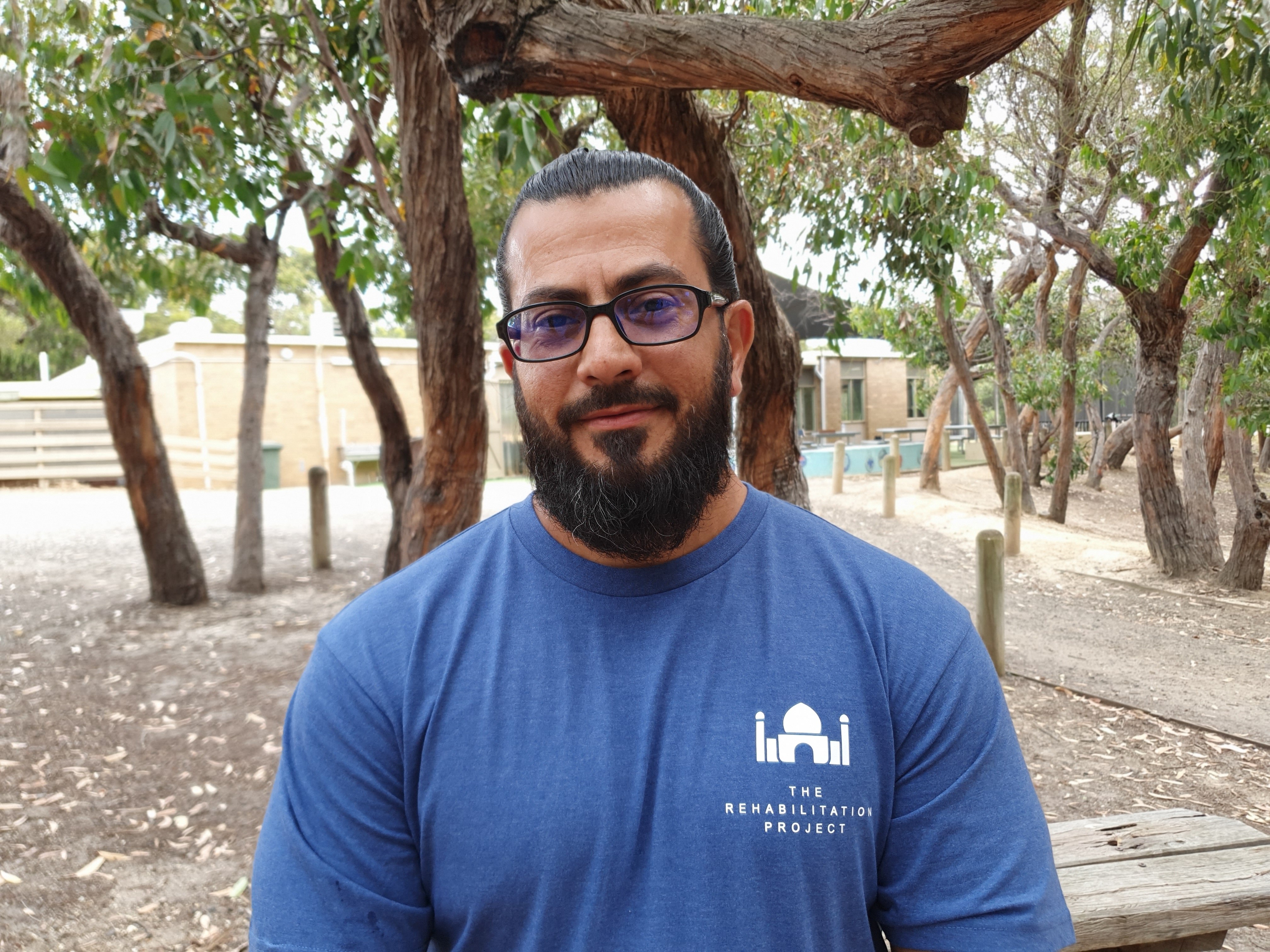 A man wearing glasses standing in front of trees