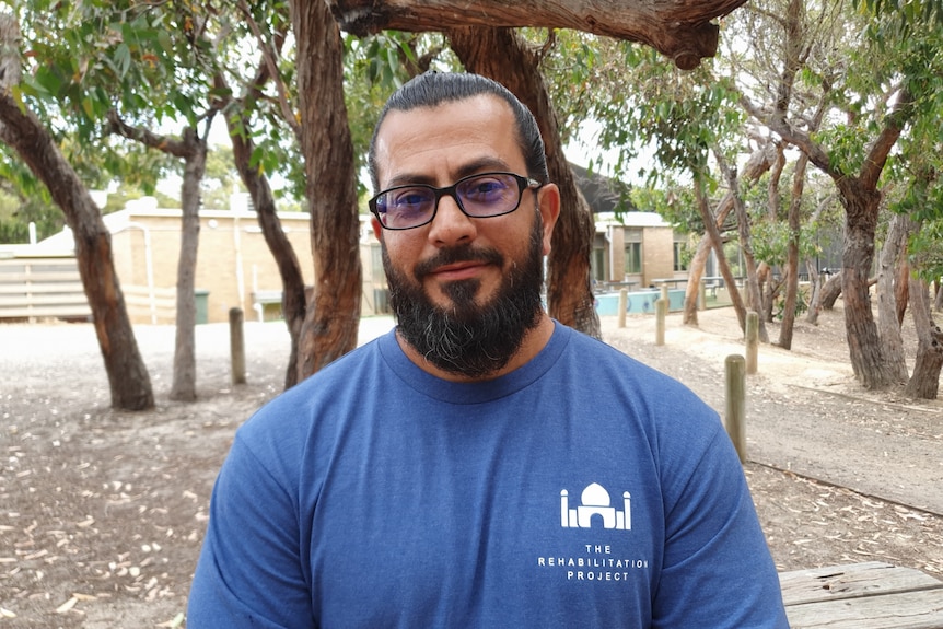 A man wearing glasses standing in front of trees