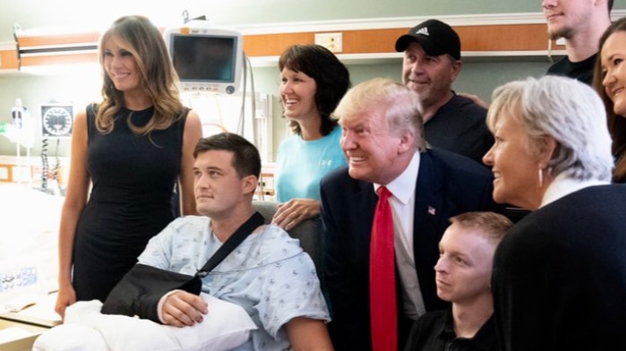 A crowd surrounds a hospital patients holding hands including President Donald Trump and first lady Melania Trump.