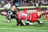 An NRL player reaches out toward the tryline with the ball, as an opponent tries to hold him back.