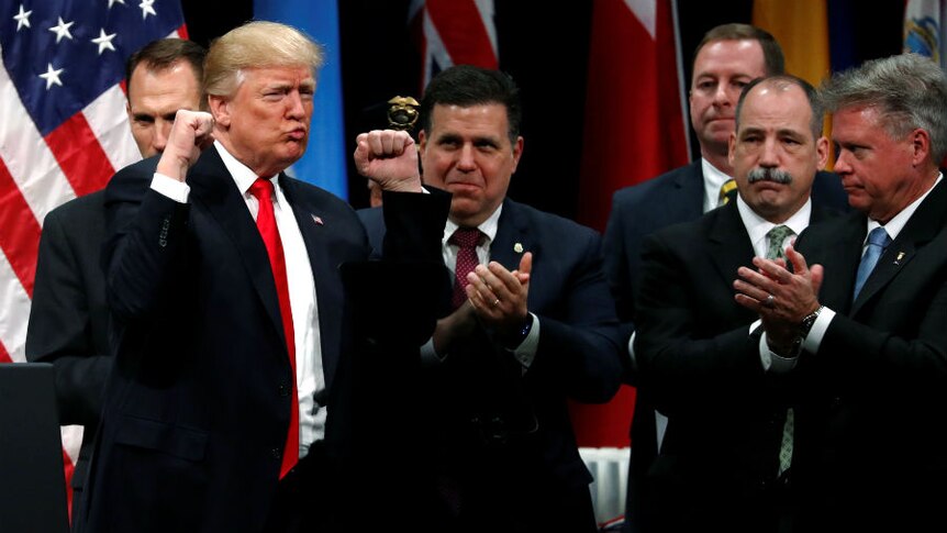 Donald Trump pumps his fists has he is applauded by a group of men in suits.