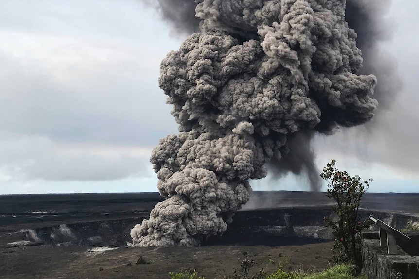 Ash column rises from the crater at Kilauea in Hawaii. It is very tall and dark.