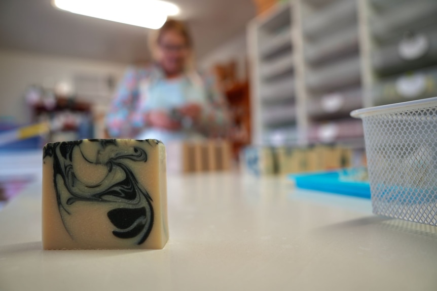 A block of soap sits on a table with a woman out of focus in the background.