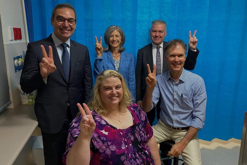 A group of people holding up two fingers as a 'V' for vaccination.