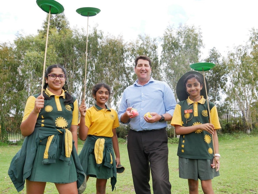 Three primary school students and a teacher on grass with circus equipment.