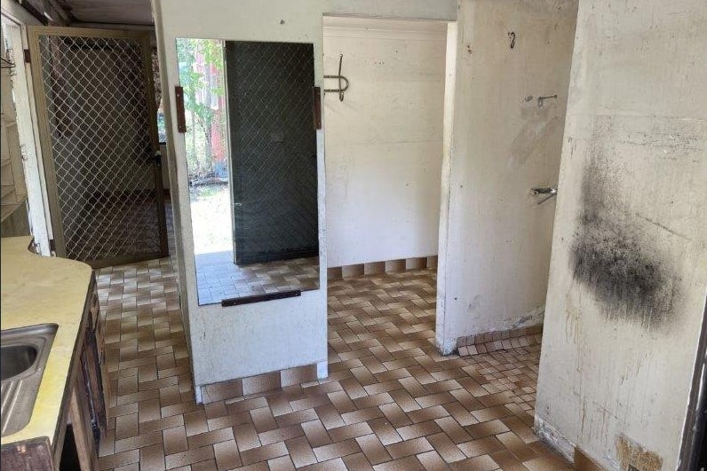 The inside of a bathroom with very aged tiles, marked walls, and a mirror