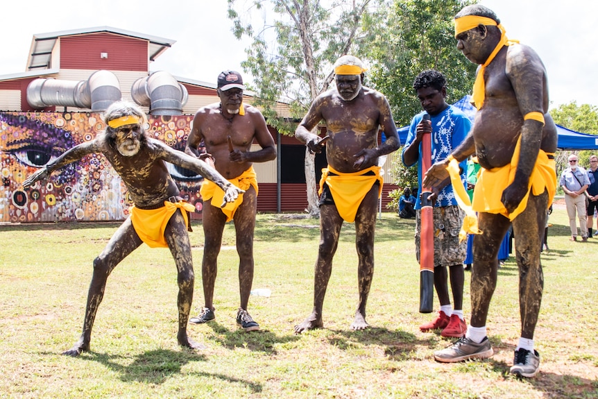 A group of Indigenous Australians dance in traditional costume and body paint.