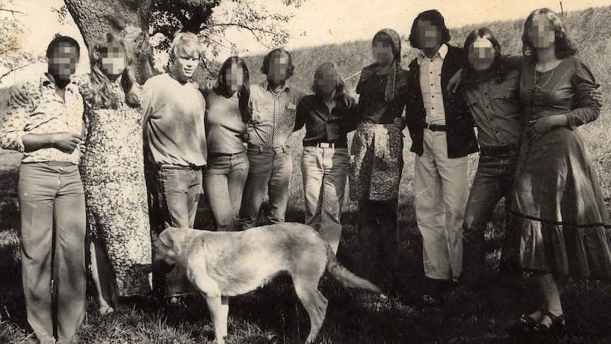 A black and white photo of happy young people standing a long line with linked arms.