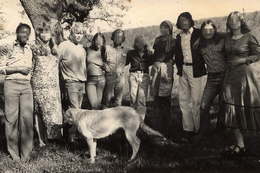 A black and white photo of happy young people standing a long line with linked arms.