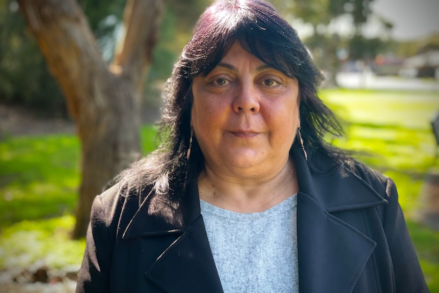 A portrait of Cheryl Axulby looking at the camera, standing in a place that looks like a lush green park.