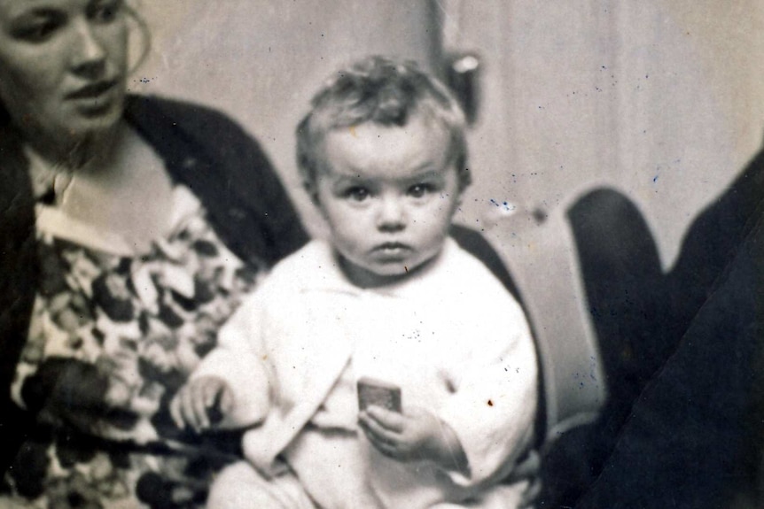 A baby sits on her mother's knee in a black and white photo.