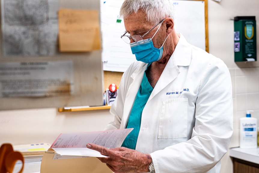 Doctor wearing scrubs and face masks reading medical reports.