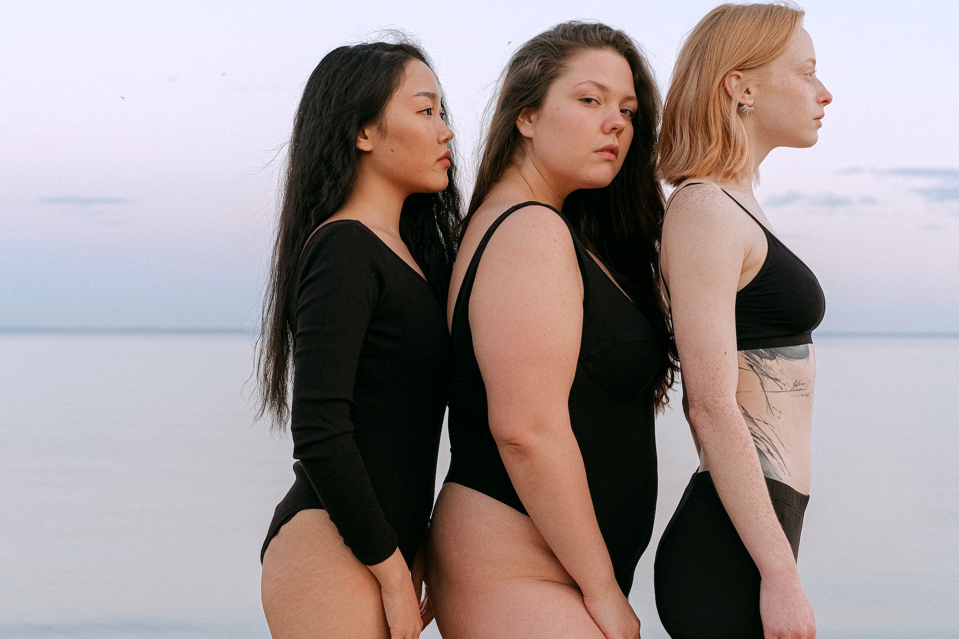 三个女人，身材不同，穿着黑色衣服，站在沙滩上。