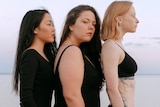 Three women, of different sizes, wearing black and standing on beach.