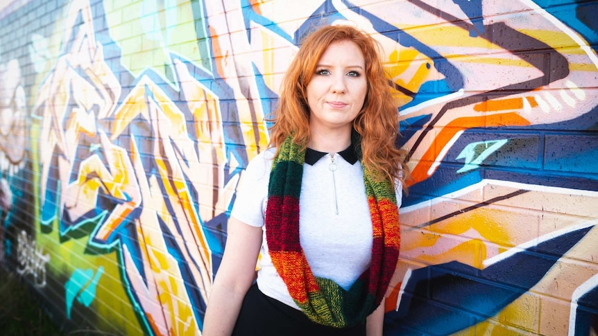 A woman with red hair leans against a mural